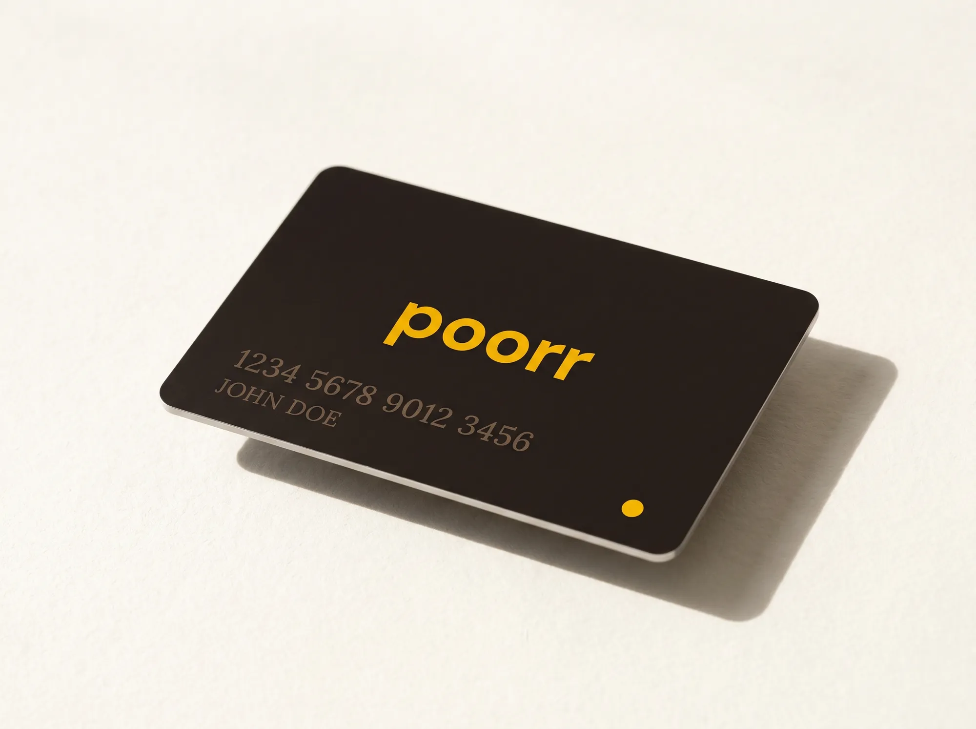 Poorr Metal Debit Card — A matte-finish metal debit card, 85.6 × 54 mm, face in solid warm charcoal (#1F1815) with the 'Poorr' wordmark laser-etched in citrus yellow (#F5B800) DM Sans. Card number and name debossed in Lora small caps. The back carries a single printed line in DM Sans: 'For the not-yet-rich.' No gradient, no hologram, no cool-blue fintech posturing.
