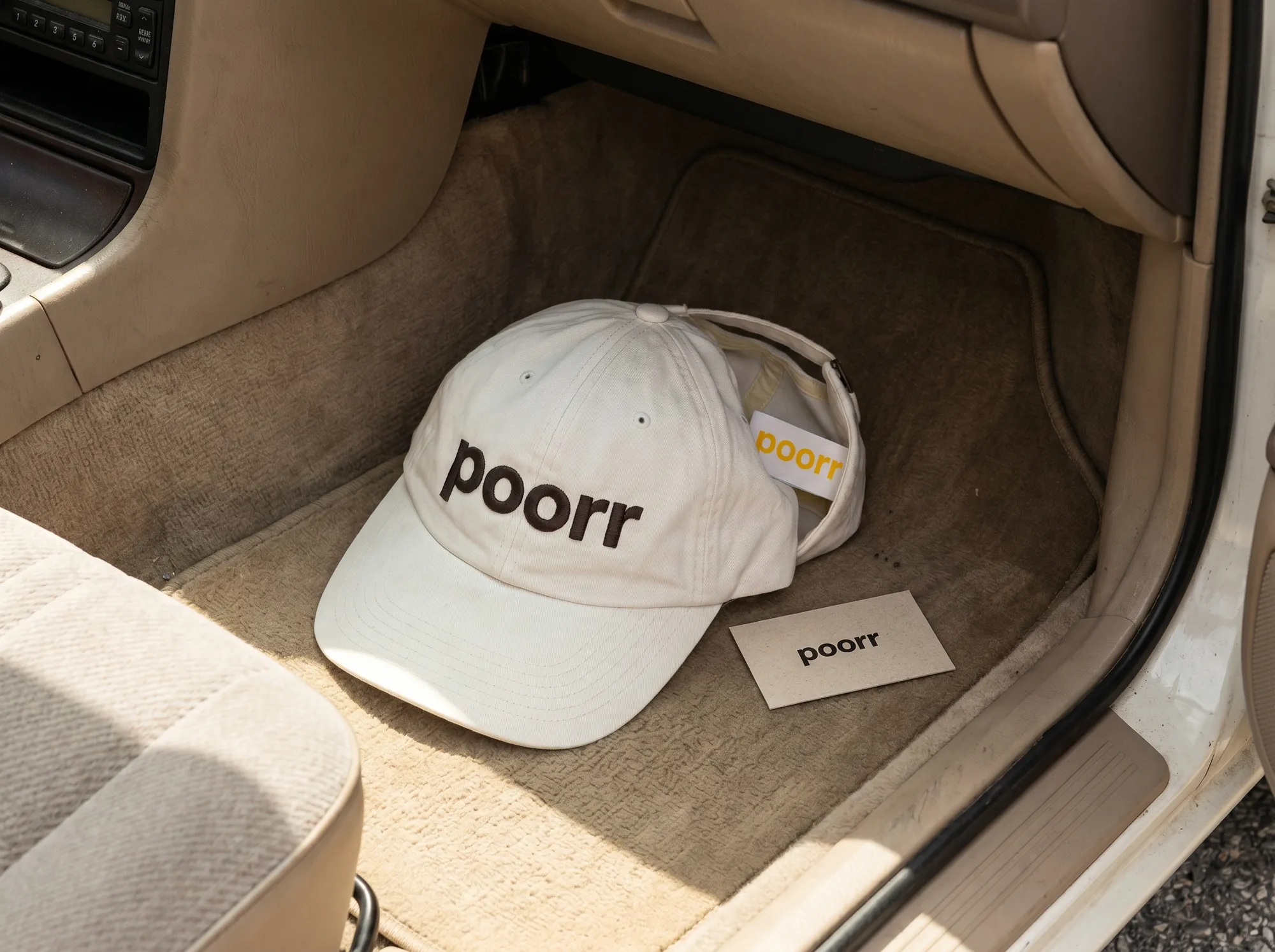 Poorr Driver Cap (Apparel) — A washed warm off-white cotton cap with the wordmark embroidered in warm charcoal — for gig drivers who'd like a small confirmation that the platform is on their side.
