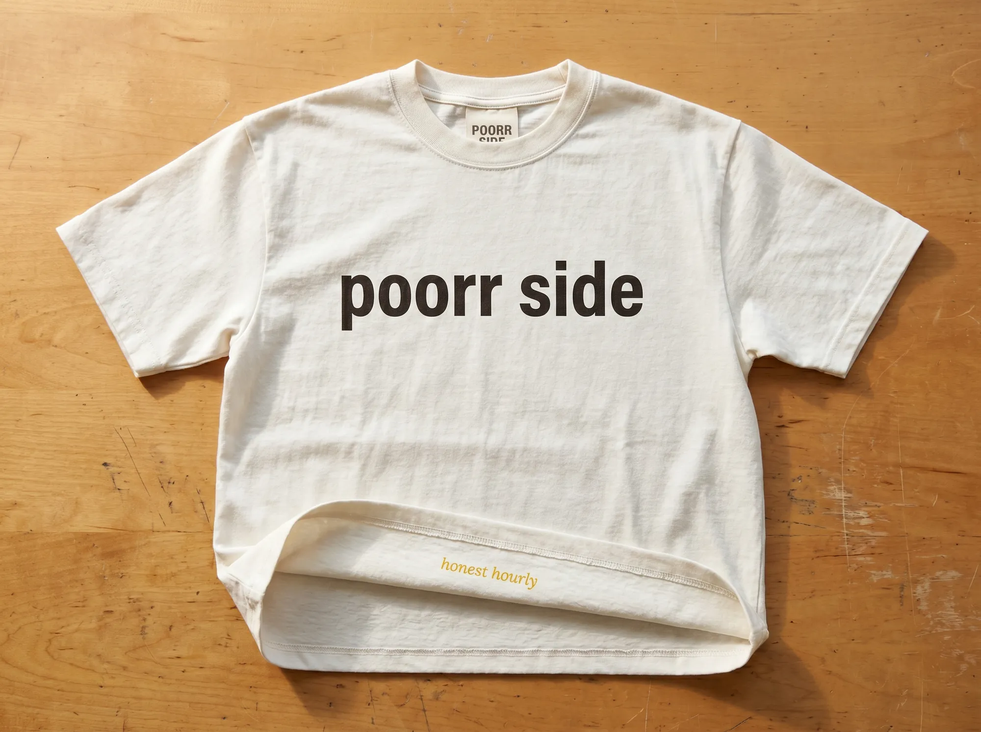 Poorr Side Tee (Apparel) — A heavyweight cream cotton tee with the wordmark in warm charcoal and a small Lora italic line at the hem reading 'honest hourly.' For Side subscribers.